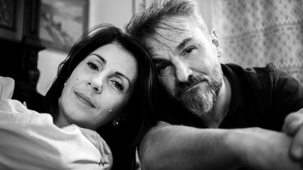 Black and white portrait of a middle-aged couple resting their heads together, showing quiet intimacy and emotional closeness at home