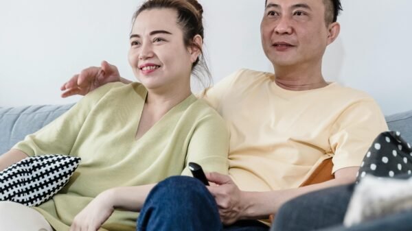 Middle-aged couple relaxing together on a sofa at home, smiling and watching television in a cozy living room