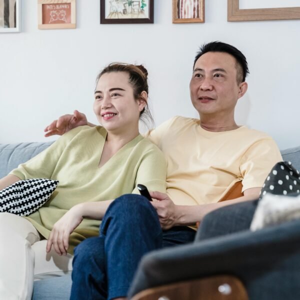 Middle-aged couple relaxing together on a sofa at home, smiling and watching television in a cozy living room