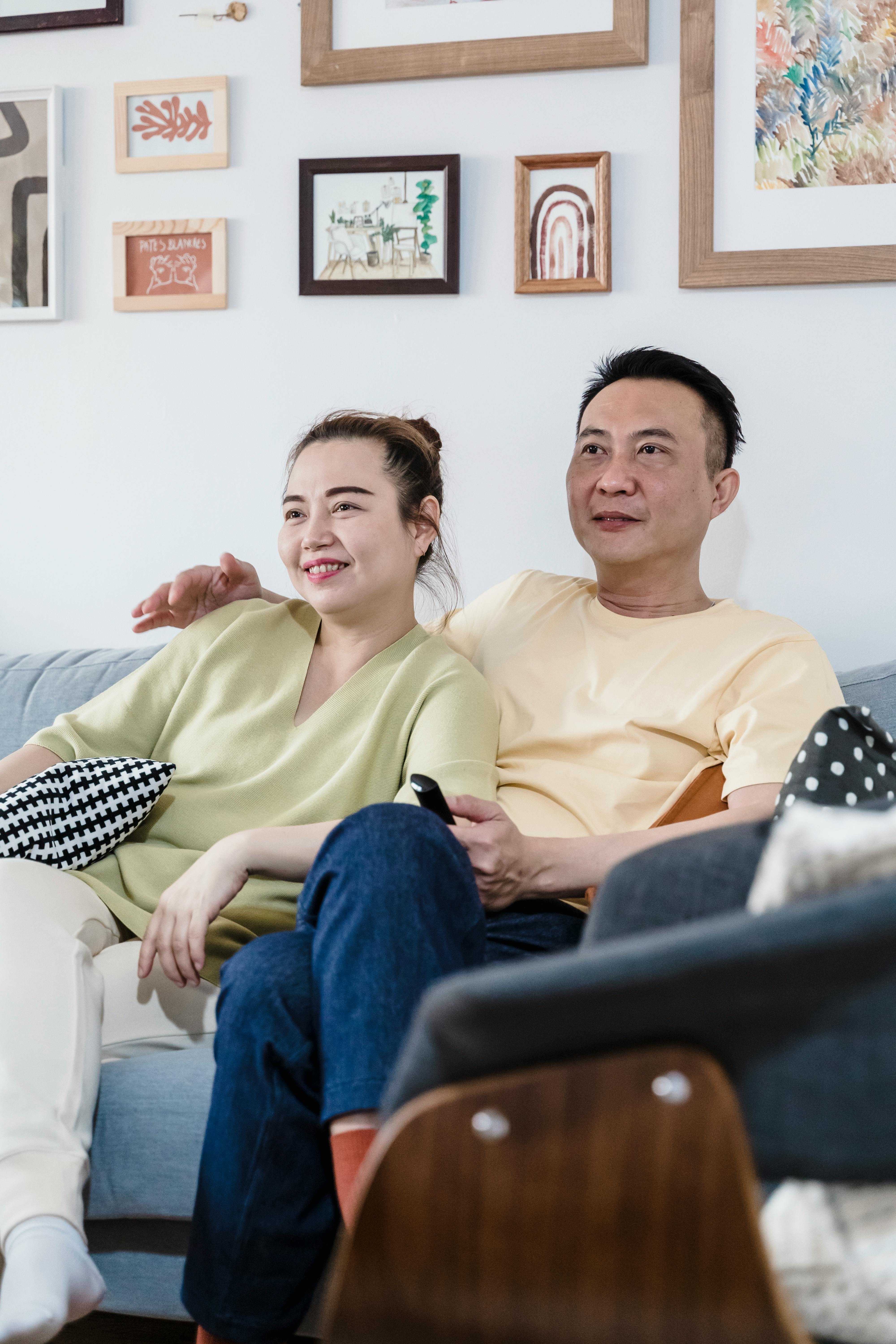 Middle-aged couple relaxing together on a sofa at home, smiling and watching television in a cozy living room