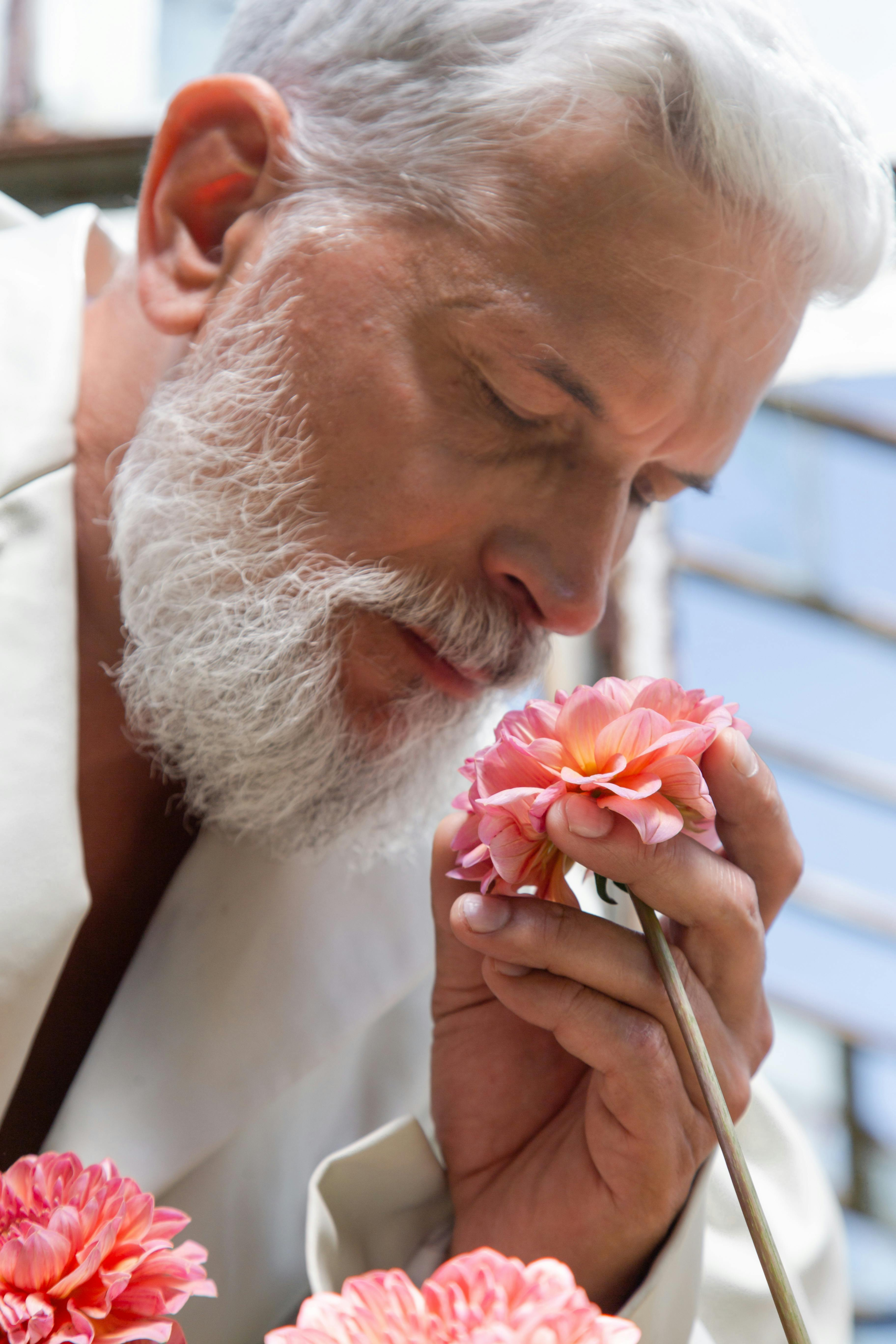 Older man with white beard gently smelling a pink flower, reflecting on love and second chances later in life