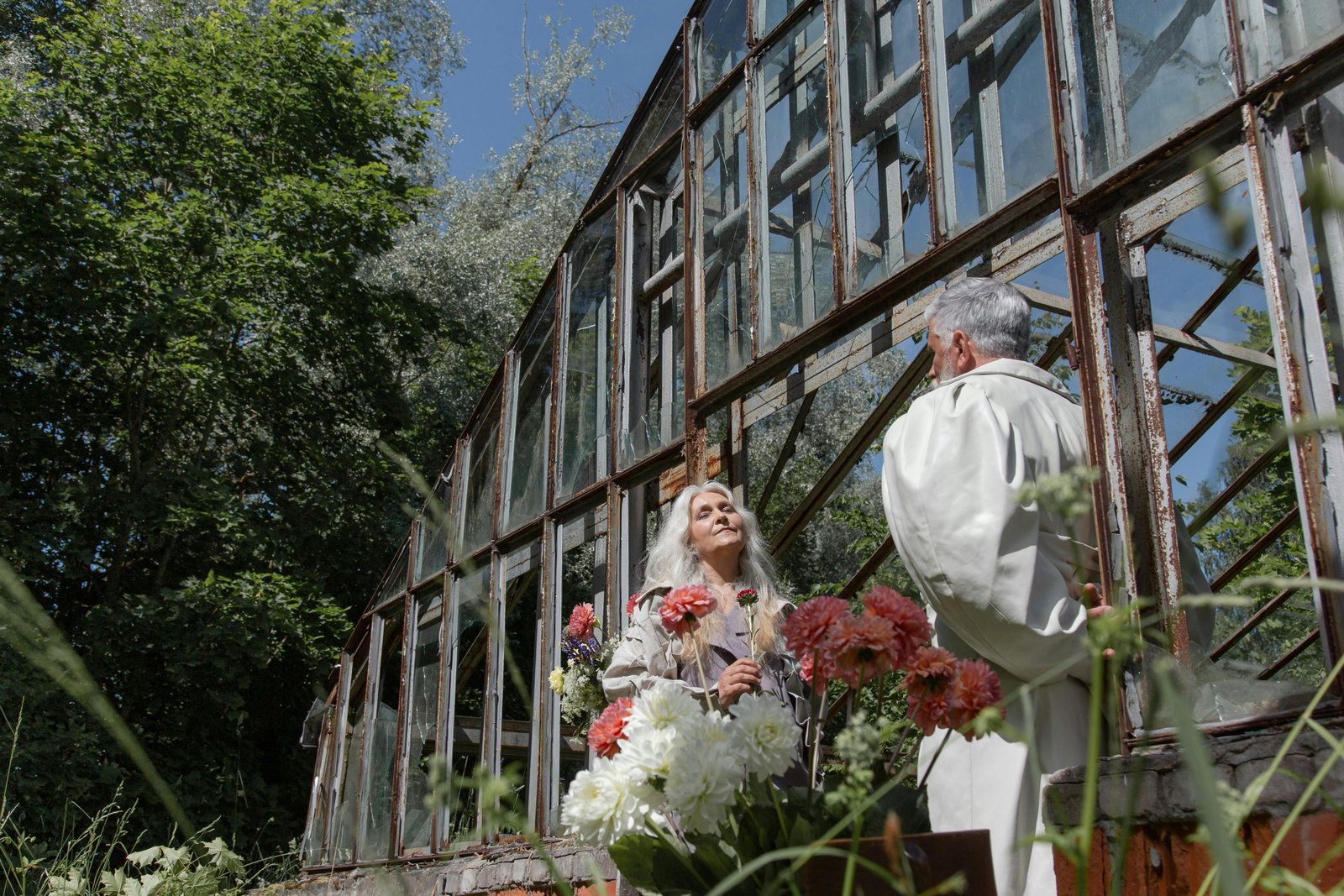 Older couple standing together near a greenhouse, sharing a calm moment of connection without words