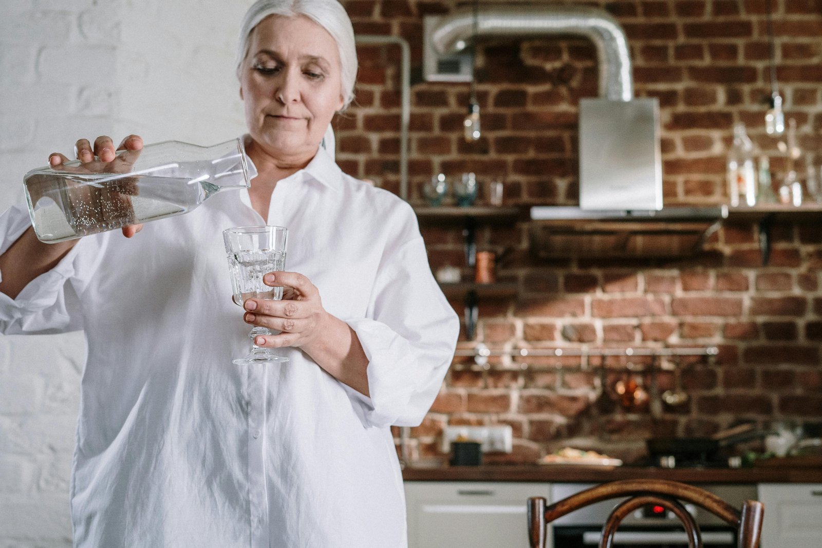 Older woman pouring a glass of water in her kitchen, practicing a simple self-care moment at home