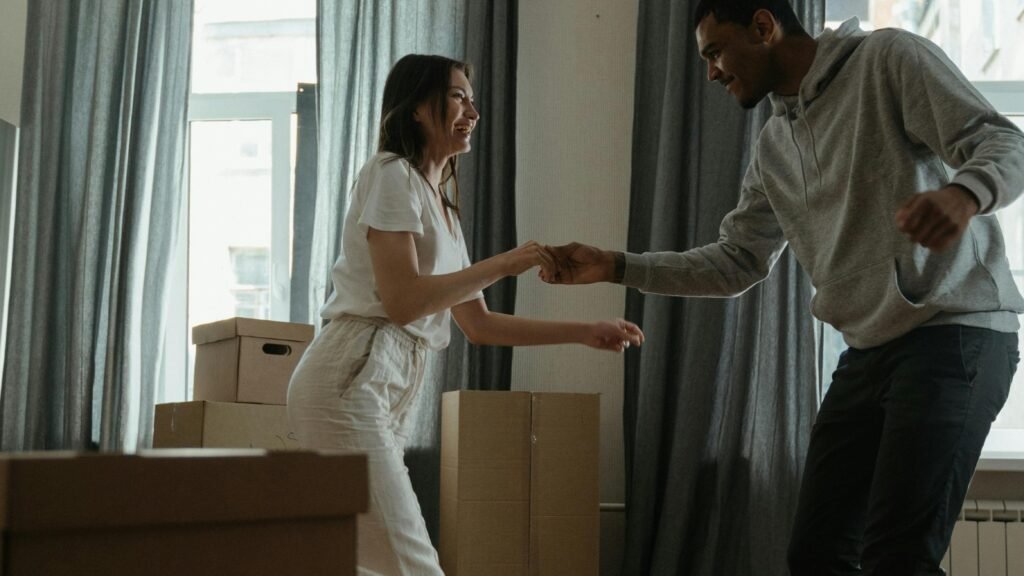 Couple dancing together in a new home surrounded by moving boxes, sharing a light and intimate moment during a life transition