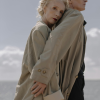 Older couple embracing near the ocean, wearing classic coats and looking thoughtful