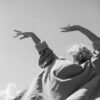 Older adult with arms raised against the sky, wearing flowing clothing and expressing freedom, movement, and presence