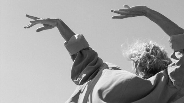 Older adult with arms raised against the sky, wearing flowing clothing and expressing freedom, movement, and presence