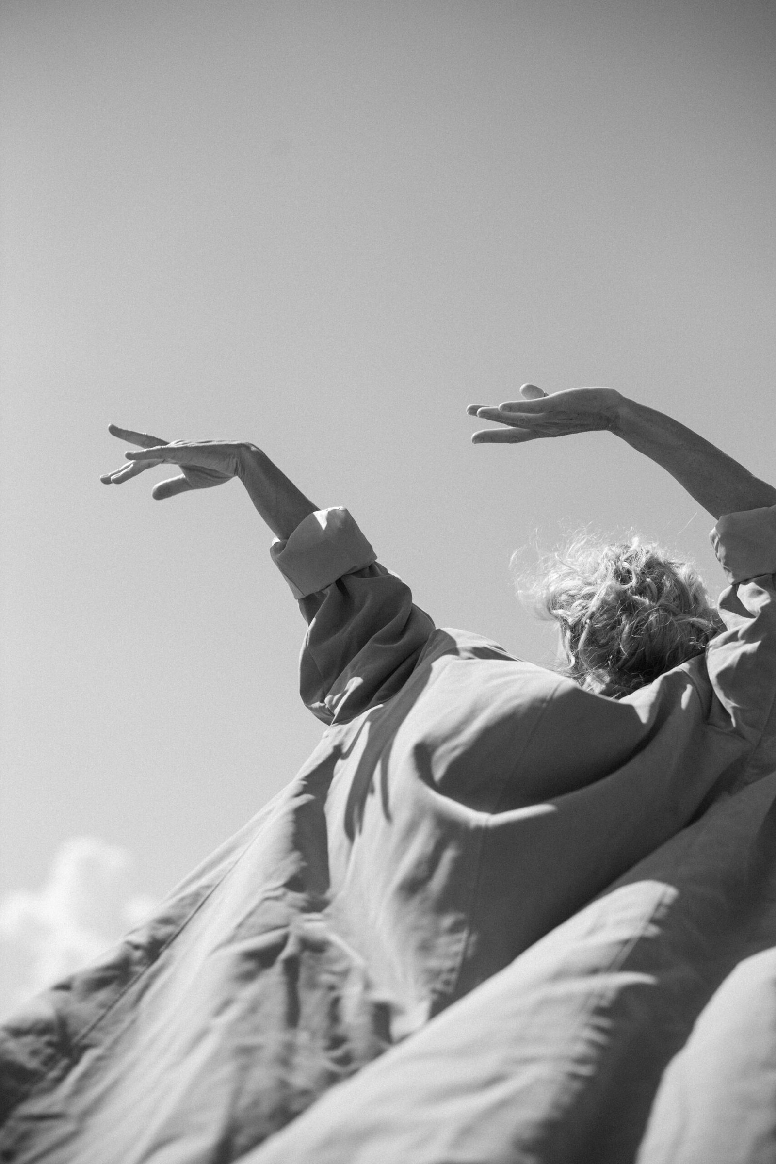 Older adult with arms raised against the sky, wearing flowing clothing and expressing freedom, movement, and presence