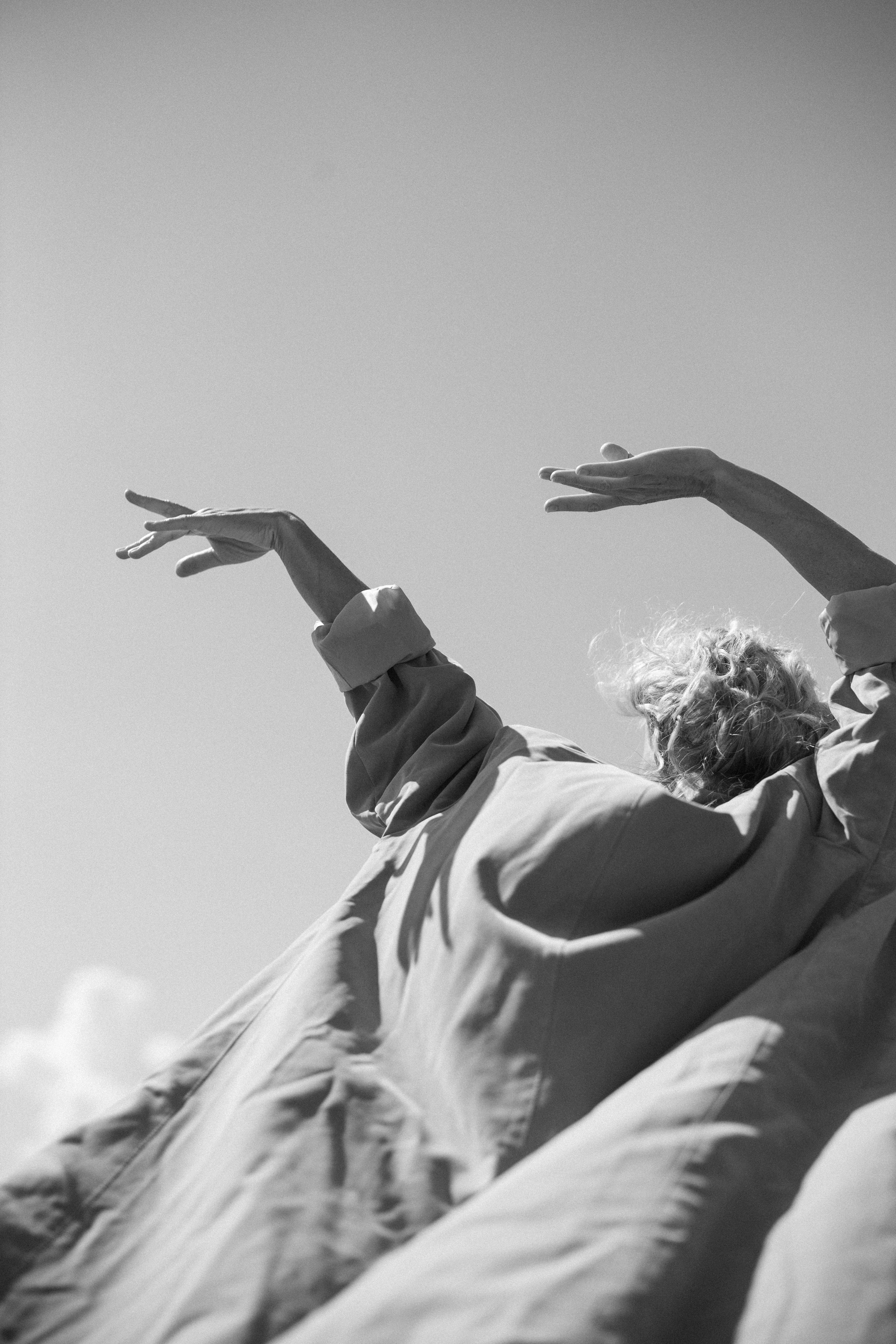 Older adult with arms raised against the sky, wearing flowing clothing and expressing freedom, movement, and presence