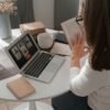 Woman in her 50s reading a book while attending a video call at home, balancing fewer tools and intentional work