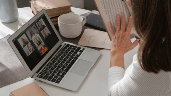 Woman in her 50s reading a book while attending a video call at home, balancing fewer tools and intentional work