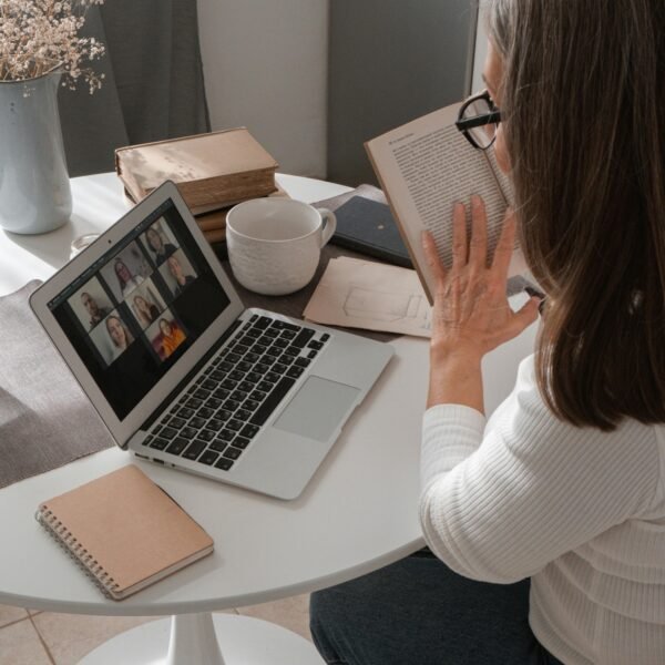 Woman in her 50s reading a book while attending a video call at home, balancing fewer tools and intentional work