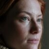 Woman in her 50s with red hair gazing thoughtfully, representing quiet confidence and inner strength