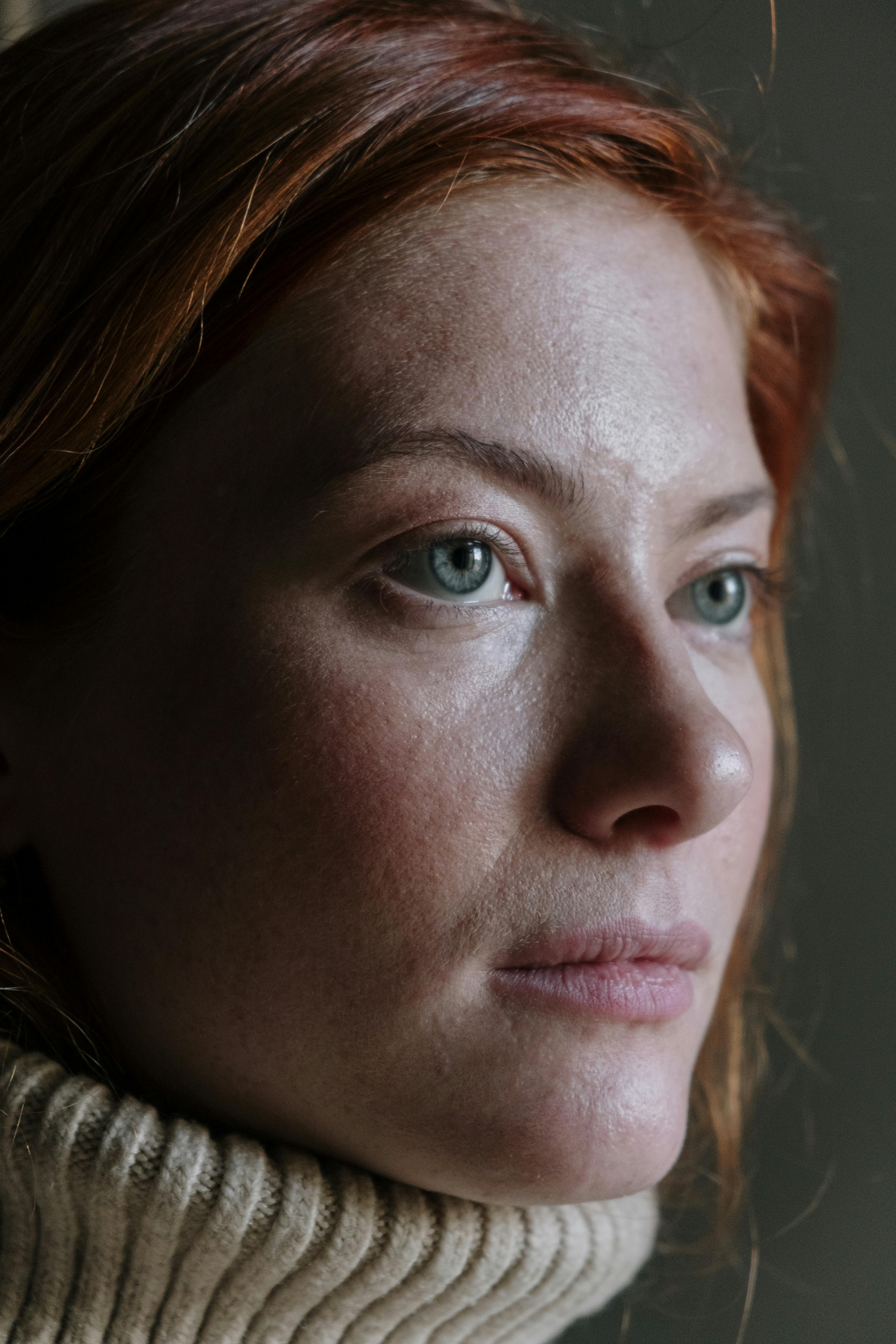 Woman in her 50s with red hair gazing thoughtfully, representing quiet confidence and inner strength