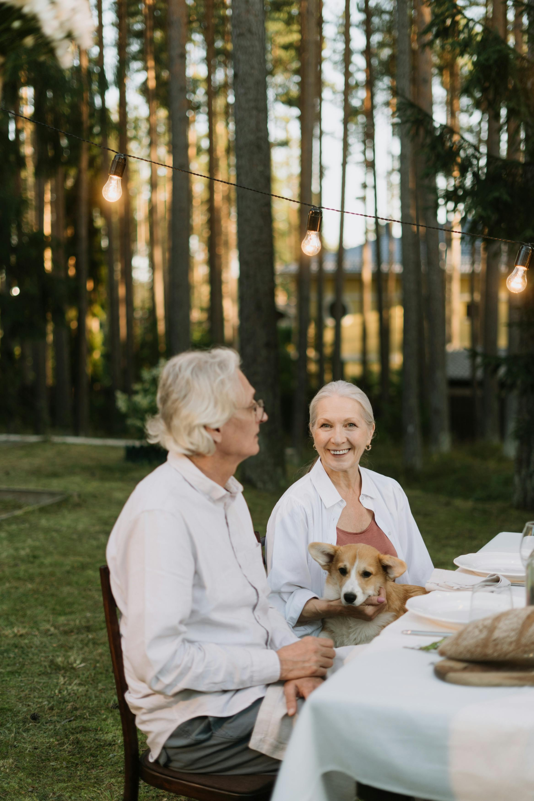 Older couple sitting at an outdoor table with their dog, enjoying a relaxed moment of connection and companionship