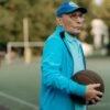 Older man standing on an outdoor basketball court holding a basketball, reflecting focus, experience, and lifelong connection to sport
