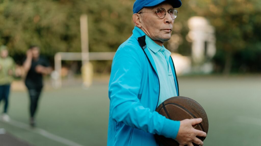 Older man standing on an outdoor basketball court holding a basketball, reflecting focus, experience, and lifelong connection to sport