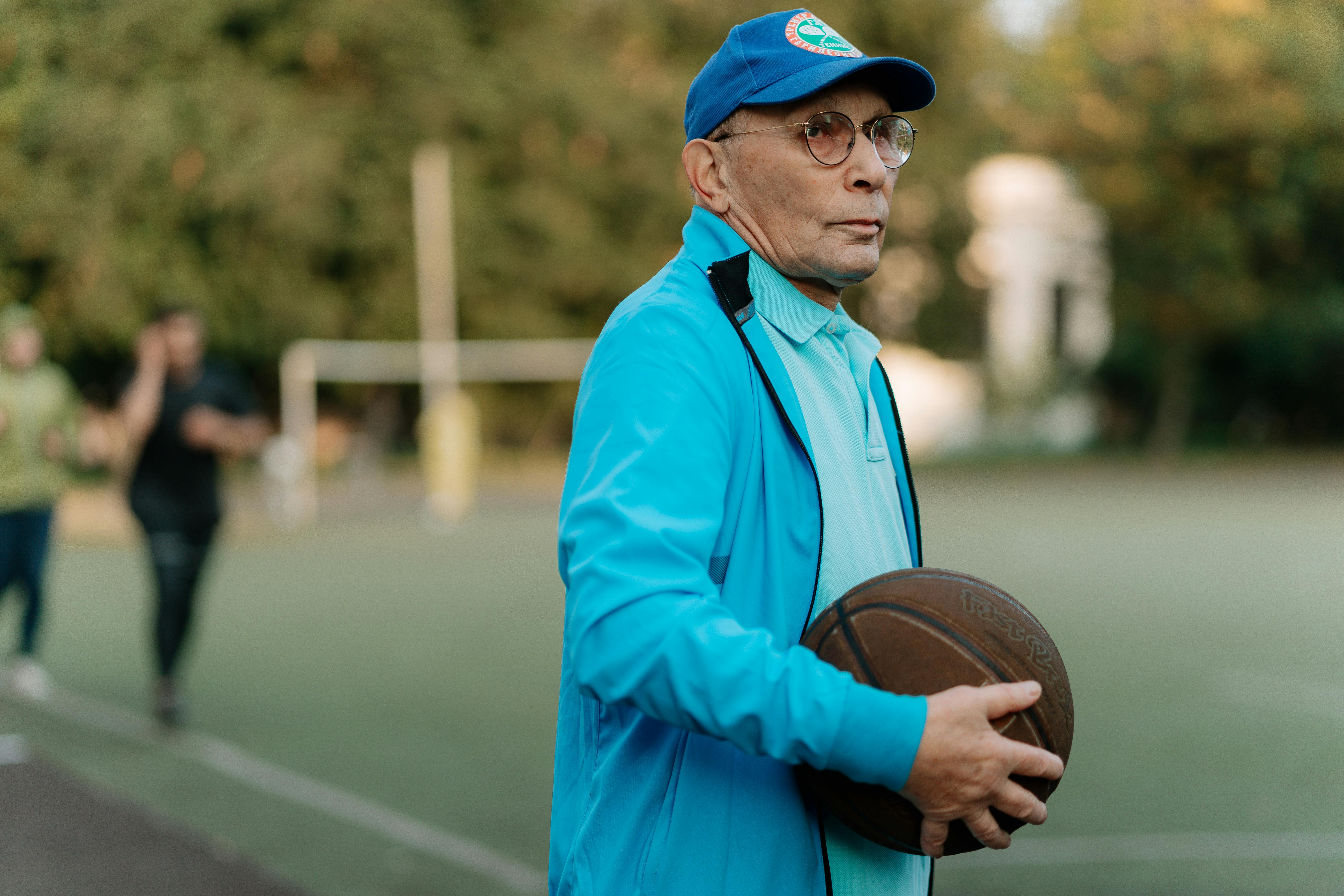 Older man standing on an outdoor basketball court holding a basketball, reflecting focus, experience, and lifelong connection to sport