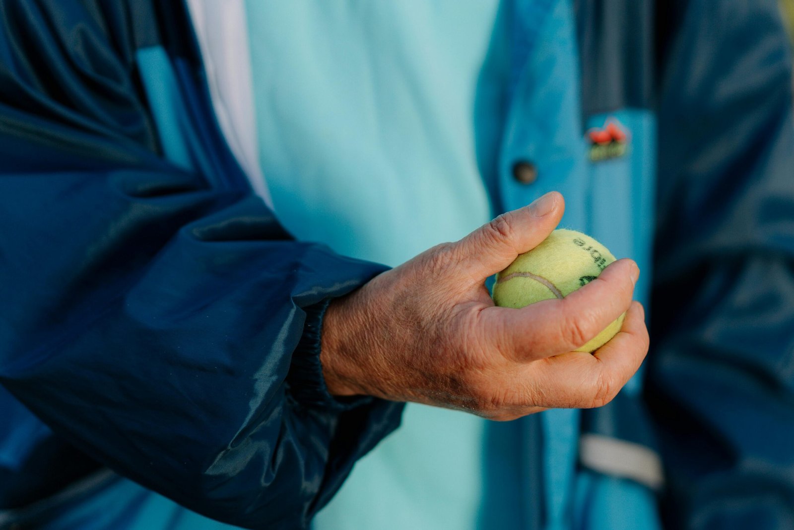 Close-up of older hands holding a tennis ball, symbolizing routine, familiarity, and mindful engagement with sport