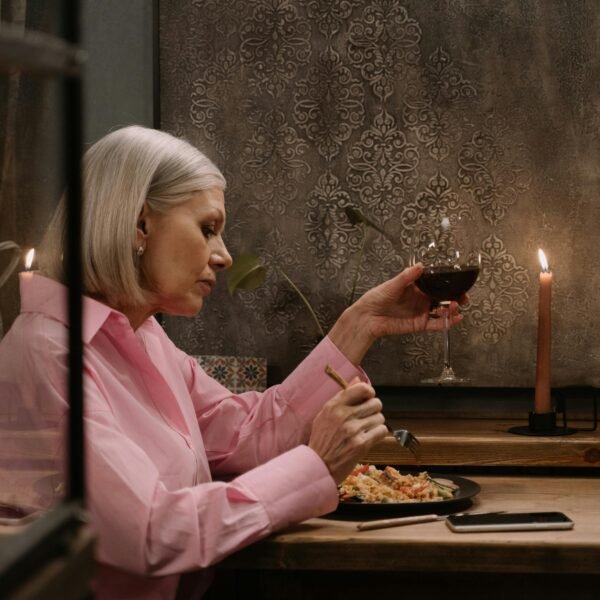 Older woman enjoying a quiet dinner with a glass of wine and candlelight, expressing calm presence and self-care