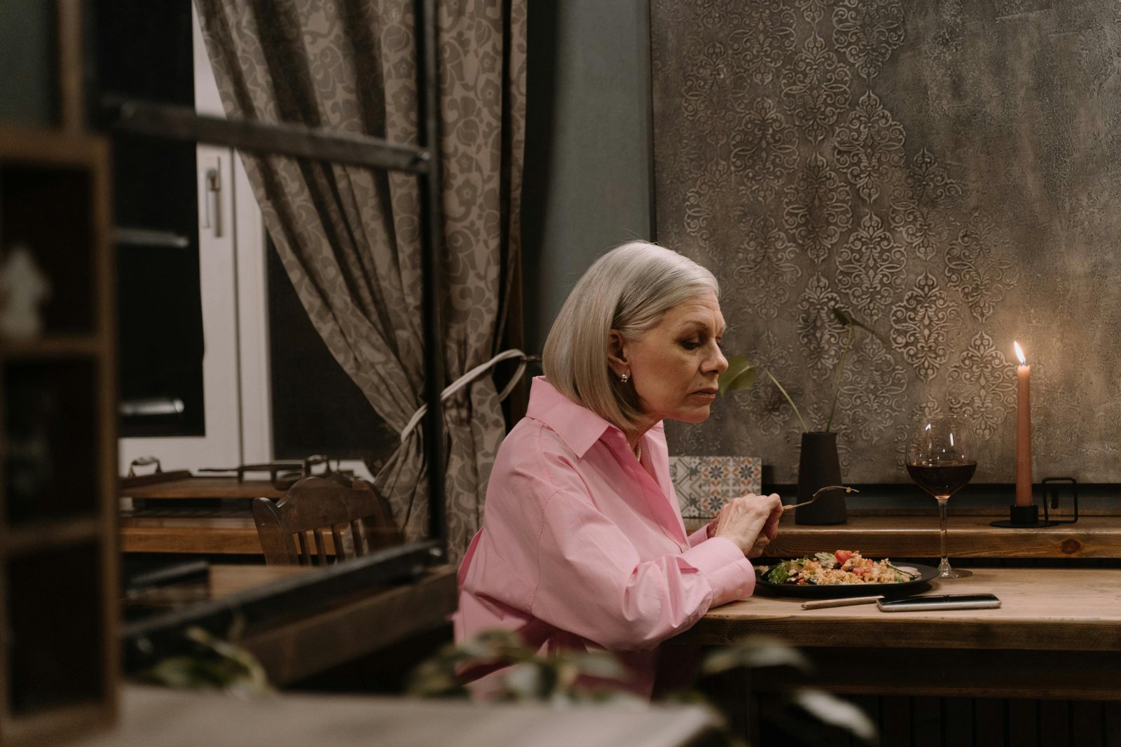 Older woman eating dinner alone at a wooden table with candlelight, creating a calm and reflective evening atmosphere