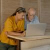 Older couple standing together at a table, looking at a laptop and discussing something thoughtfully at home