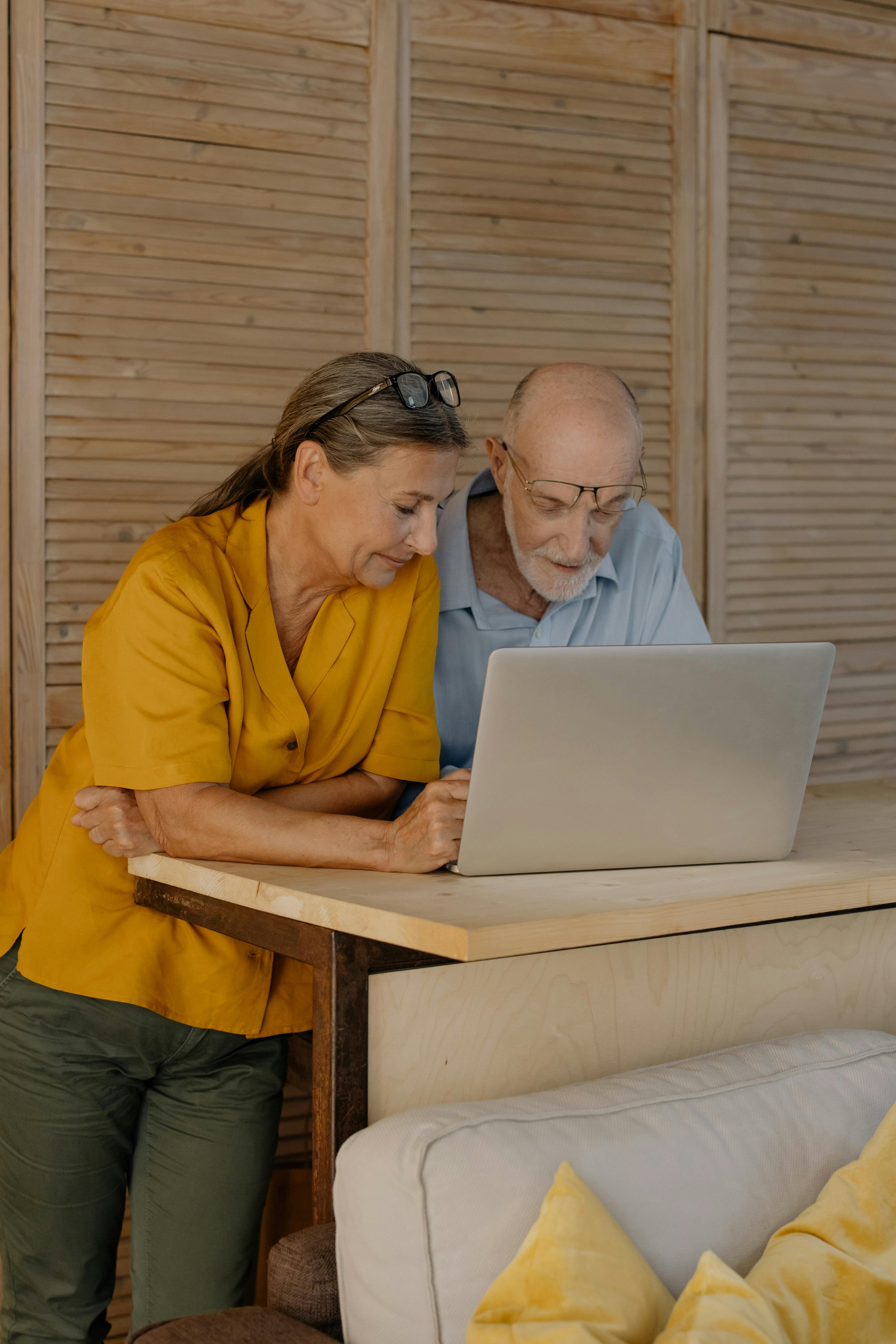 Older couple standing together at a table, looking at a laptop and discussing something thoughtfully at home