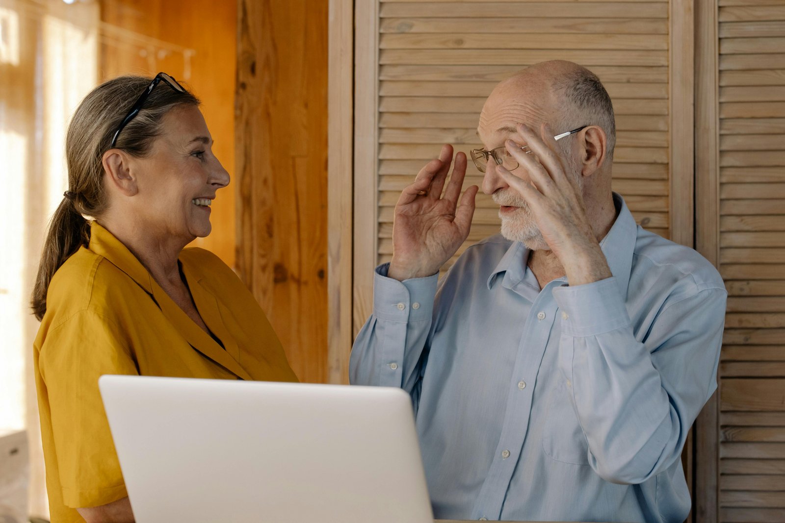 Older couple smiling and talking beside a laptop, showing connection, communication, and mutual support
