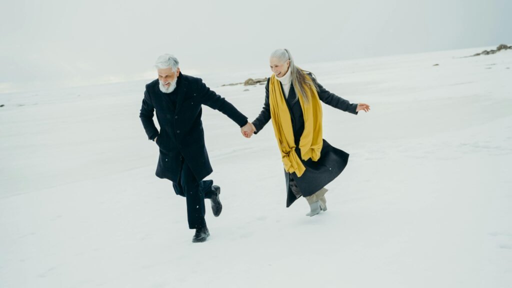 Older couple holding hands while walking across a snowy landscape, symbolizing connection and companionship in midlife