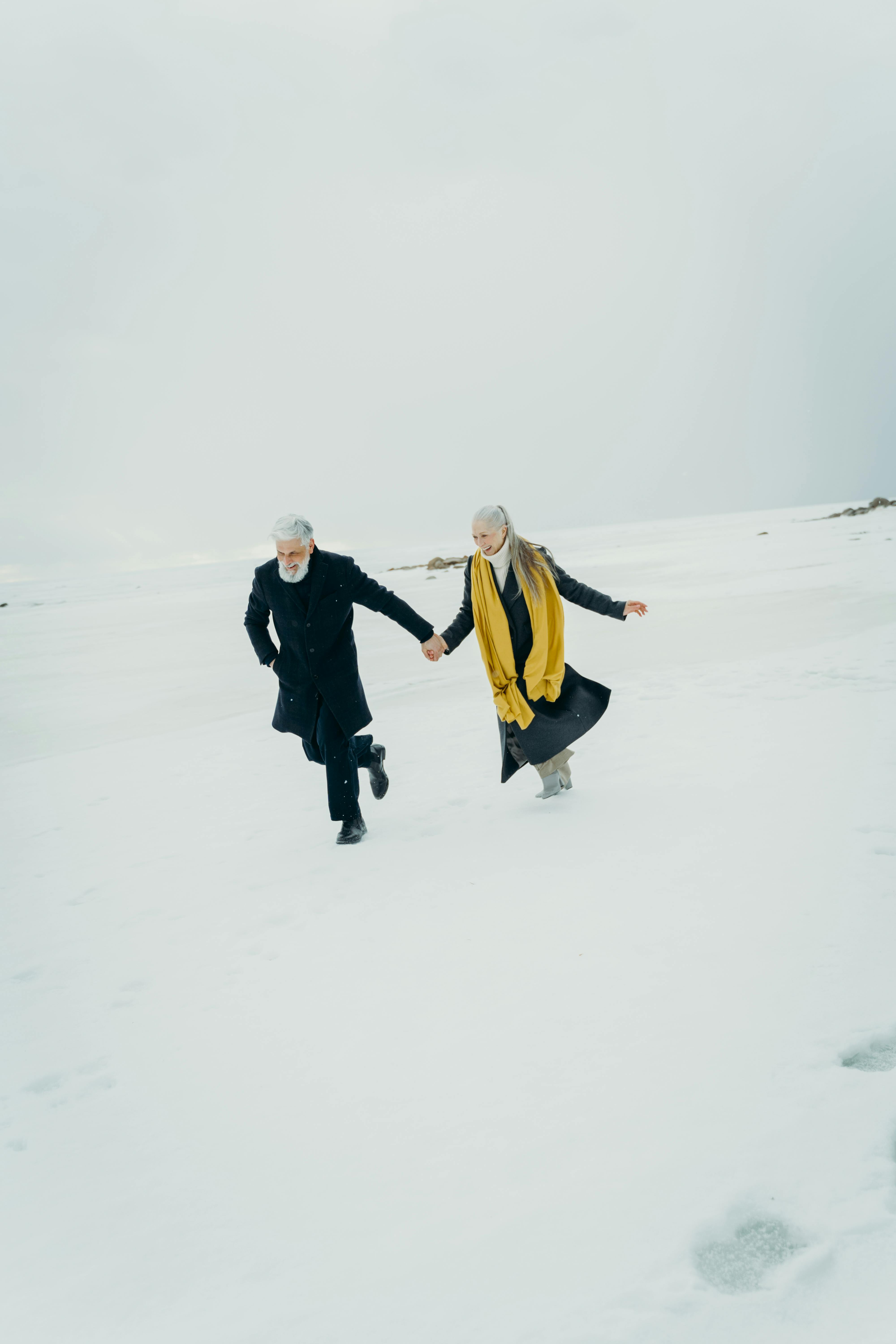 Older couple holding hands while walking across a snowy landscape, symbolizing connection and companionship in midlife