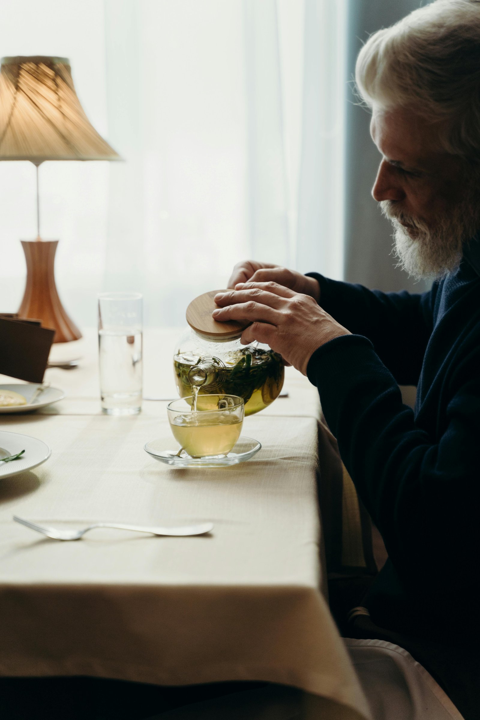 Older man pouring tea at a table, enjoying a slow, intentional moment later in life