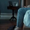 Older man sitting quietly at home, feet in slippers, reflecting in a calm, dimly lit room