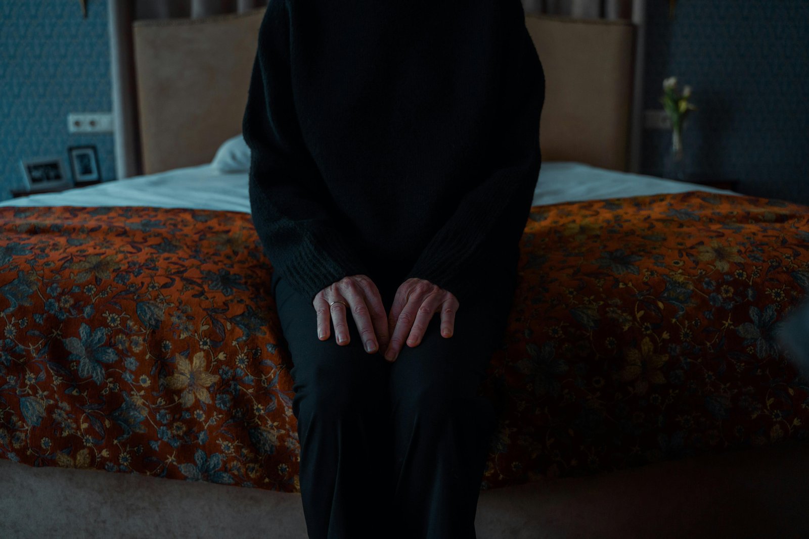 Older adult sitting on a bed with hands folded, symbolizing grief, solitude, and emotional awareness with age