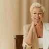 Confident middle-aged woman with short blonde hair and glasses, smiling while seated in a neutral-toned modern interior