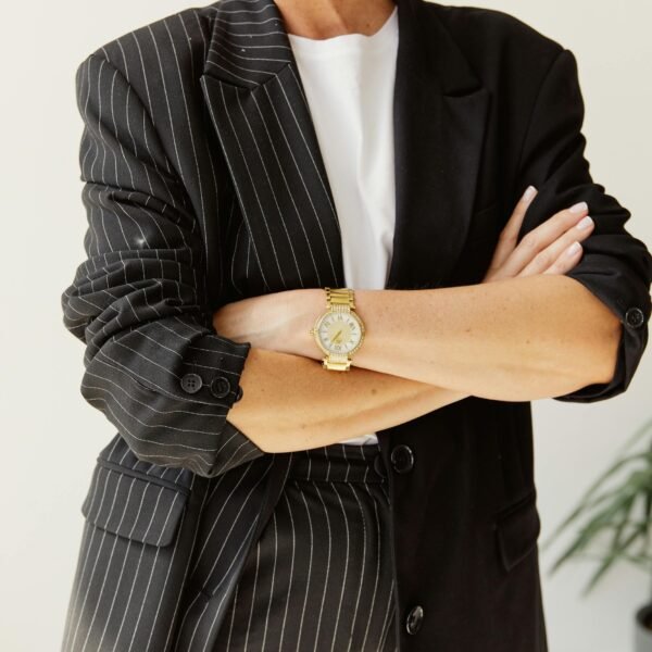 Confident woman in her 40s wearing a black pinstripe suit with arms crossed, expressing quiet authority and self-assurance