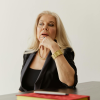 Thoughtful middle-aged woman sitting at a desk with a notebook, pausing while considering an important choice