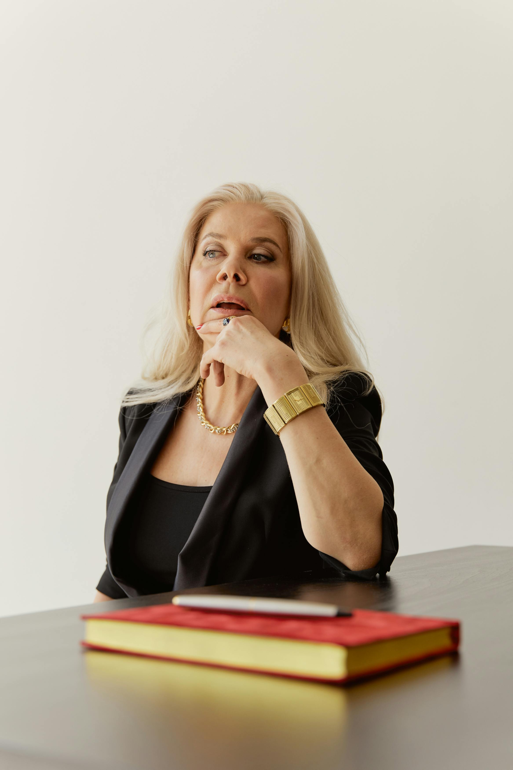 Thoughtful middle-aged woman sitting at a desk with a notebook, pausing while considering an important choice
