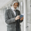 Older man reading a book while standing with luggage in a modern airport hallway