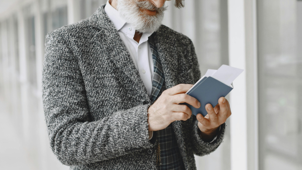 Older man reading a book while standing with luggage in a modern airport hallway