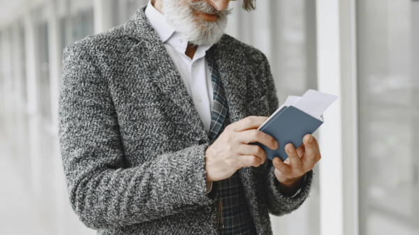 Older man reading a book while standing with luggage in a modern airport hallway