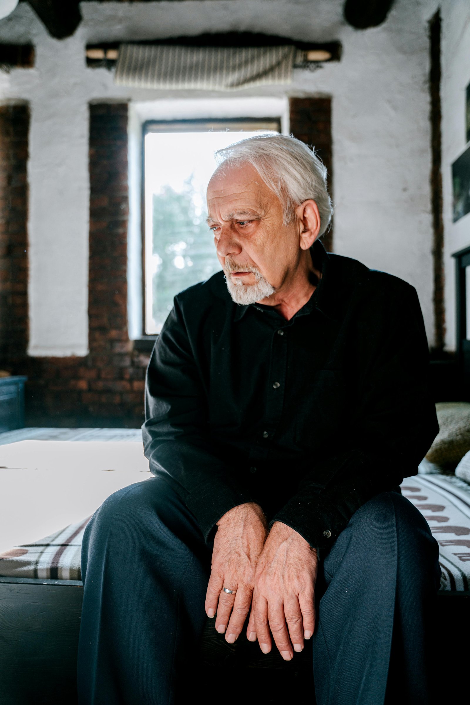 Senior man sitting on a bed holding a photo frame, wiping tears while processing deep emotions