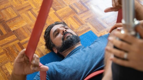 Man in his 40s lying on a mat during a guided stretch session, using resistance bands in a calm indoor space