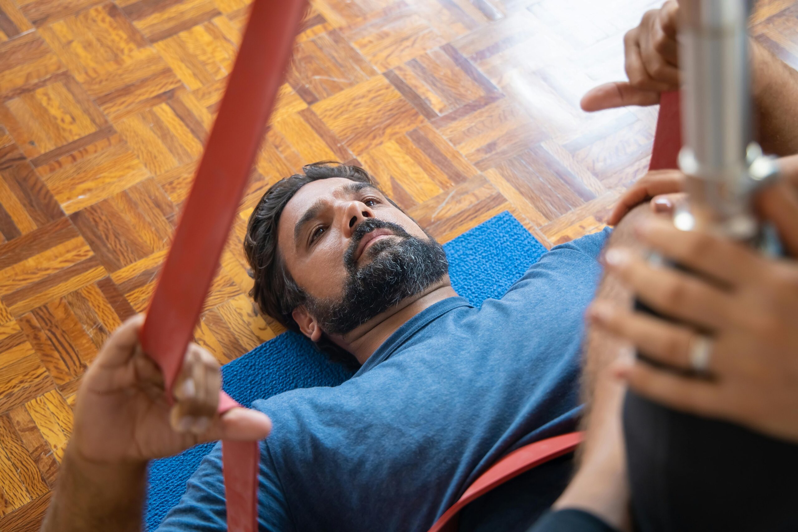 Man in his 40s lying on a mat during a guided stretch session, using resistance bands in a calm indoor space
