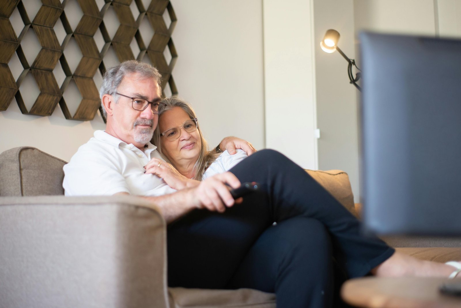 Middle-aged couple sitting close together on a couch, watching television and sharing a calm, restful moment