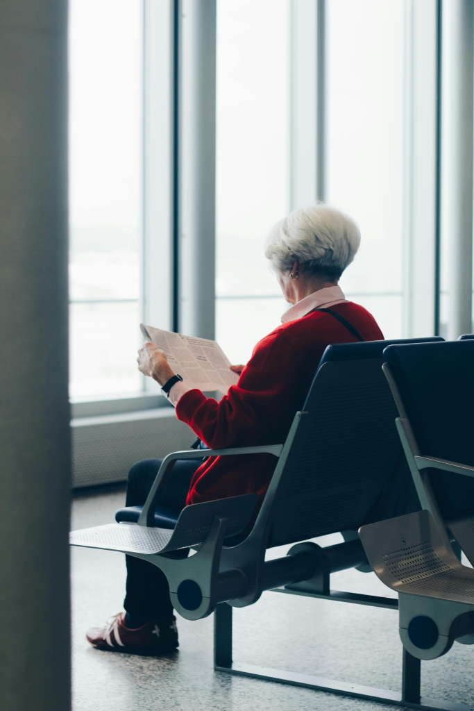 Older woman sitting in an airport terminal reading a newspaper during solo travel