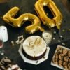 Elegant 50th birthday celebration setup with gold number 50 balloons, cake, desserts, and festive table decor