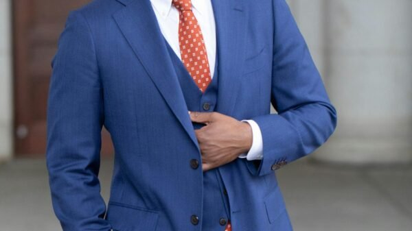 Smiling man wearing a blue suit and red tie, standing confidently outdoors in a professional setting