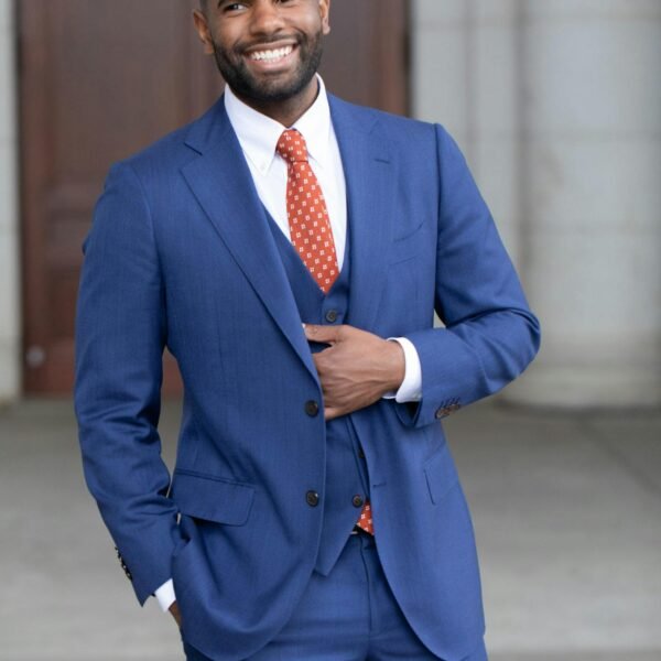 Smiling man wearing a blue suit and red tie, standing confidently outdoors in a professional setting