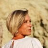Middle-aged woman with short blonde hair gazing thoughtfully into the distance, standing outdoors in warm natural light
