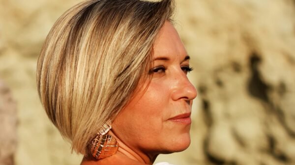 Middle-aged woman with short blonde hair gazing thoughtfully into the distance, standing outdoors in warm natural light